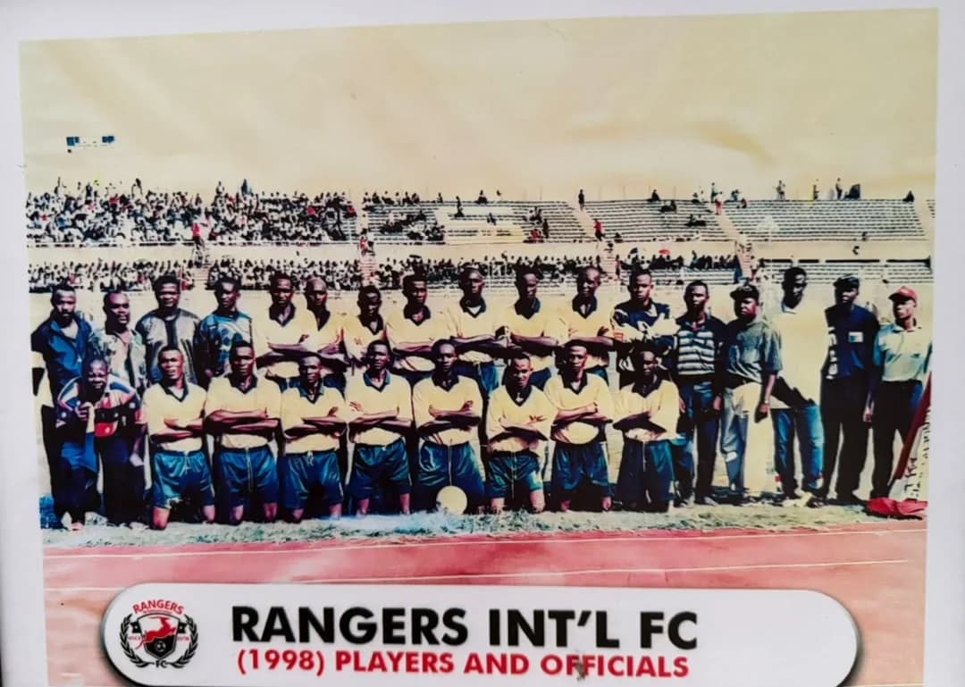 The 1998 Rangers players in yellow and blue, with officials, on the running track of a stadium.