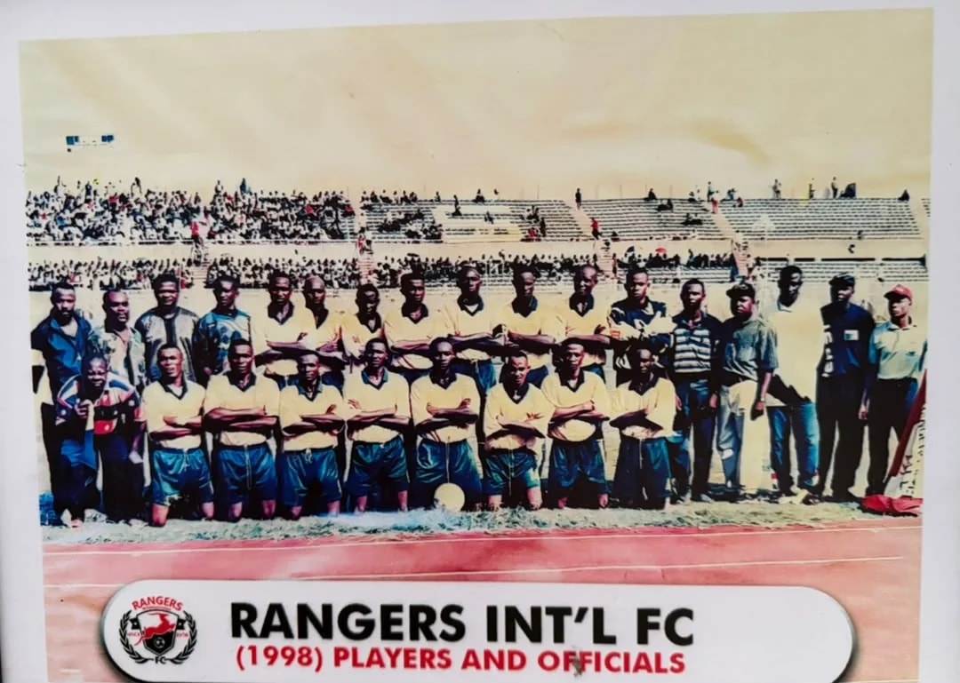 The 1998 Rangers players in yellow and blue, with officials, on the running track of a stadium.